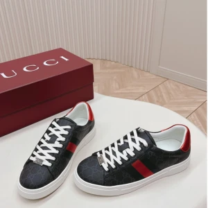 Gucci Ace sneakers svart/röd - Gucci Ace sneakers i svart skinn med diskret GG-mönster, vita snören och vit sula. Sidan har den klassiska röda och svarta randen och hälen är metallicröd. Snygg och tidlös modell med rund tå och platt sula.
