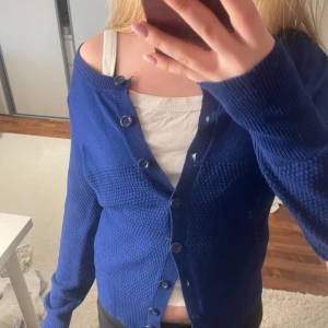 Blå kofta med knappar - Snygg blå kofta med rund halsringning och knappar hela vägen framtill. Koftan har långärmad passform och ett diskret stickat mönster över bröstet och ärmarna. Perfekt att slänga över en topp för en chill och stilren look.