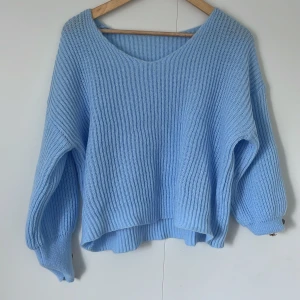 Ljusblå stickad tröja med v-ringning - Supermysig ljusblå stickad tröja med v-ringad hals och oversized passform. Tröjan har långa ärmar och ribbad struktur som ger en chill och avslappnad vibe. Perfekt att slänga på sig när det är lite kyligt ute.