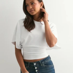 Nelly topp - Säljer en vit croppad topp med bred resår i midjan som ger en snygg siluett. Toppen har korta, vida ärmar och rund halsringning. Perfekt att styla med höga jeans för en trendig look. Storlek xs