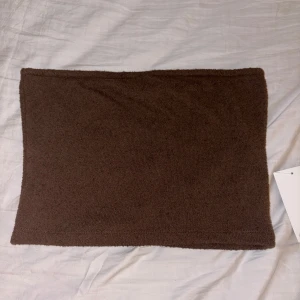 Brun stickad bandeau tubtopp - Brun bandeau tubtopp i enkel design. Perfekt att styla med jeans eller kjol för en chill och trendig look. Toppens material är mjukt och stretchigt vilket gör den bekväm att bära hela dagen. Helt oanvänd med lapp kvar.