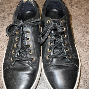 Svarta Vagabond sneakers i skinn - Svarta sneakers från Vagabond i skinn med vita sulor och svarta snören. Guldiga öljetter och snygg detalj i lack med krokopräglad look på hälen. Klassisk rund tå och platt sula, passar perfekt till streetstyle.