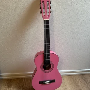 Rosa gitarr - Rosa mindre gitarr, knappt använd. Ej stämd. Nybörjar bok och stäm-instrument följer med + fodral men dragkedjan är trasig. 