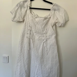 Vit kortklänning med puffärm och snörning - Superfin vit kortklänning med puffärmar och söt broderad spets. 
