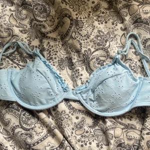 Ljusblå broderad bikini topp M - Supersöt ljusblå bikini topp med broderade blommor och små volangdetaljer längs kanten. Axelbanden är justerbara. Perfekt för dig som vill ha en feminin och trendig look. Aldrig använd