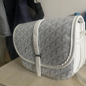 Vit axelväska med mönster  - Snygg vit axelväska med geometriskt mönster i grått. Väskan har justerbar axelrem, lock med spänne och flera fack inuti. Perfekt storlek för det viktigaste och stilren design som sticker ut.