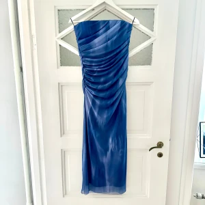Blå axelbandslös klänning  - Axelbandslös klänning i snyggt blått mönster. Övre tyglagret är mönstrat meshtyg som är draperat snyggt fram och bak på klänningen. Midilängd och aldrig använd med prislapp kvar.