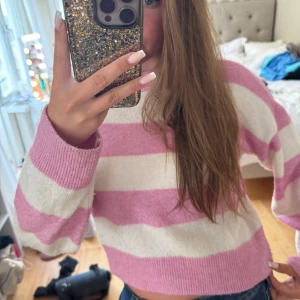 Rosa och vit randig stickad tröja - Supermysig stickad tröja med breda rosa och vita ränder. Modellen är croppad med ribbade muddar och rund hals. Perfekt för dig som gillar en chill och söt stil. Passar till jeans eller kjol för en avslappnad vibe.