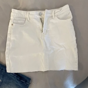 Vit jeanskjol från Amisu, strl 34 - Vit kort jeanskjol från Amisu i storlek 34. Kjolen har klassisk femficksdesign, bälteshällor och rå kant nertill för en cool vibe. Perfekt till sneakers eller boots och enkel att matcha med crop tops eller hoodies.