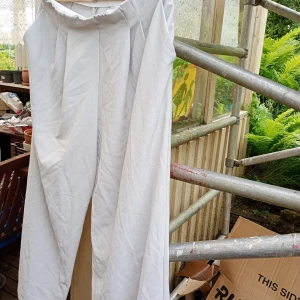 Vita vida kostymbyxor stl XL  - Snygga vita kostymbyxor med hög midja och vida ben. Byxorna har pressveck framtill och två fuskfickor bak. Perfekta för en clean och stilren look. Materialet känns som bomull eller polyesterblandning.stl XL.