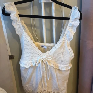 Zara slutsålt linne - Supersöt vit linnetopp från Zara med virkade detaljer och volangkant. Toppen har breda axelband med spets och en liten knytning framtill. Nederdelen är i tunn bomull med broderade blommor och spetskant. Perfekt för sommarens alla tillfällen!