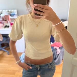 Beige topp från Gina Tricot - Supersöt beige stickad topp från Gina Tricot med puffiga korta ärmar. Modellen är croppad och sitter snyggt på kroppen. 
