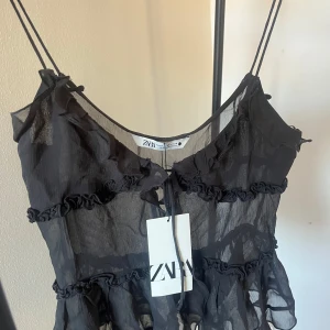 Svart volangtop från Zara -  Svart linnetopp från Zara med tunna axelband och  volanger. Helt ny med prislappen kvar, hör av dig för fler frågor😇