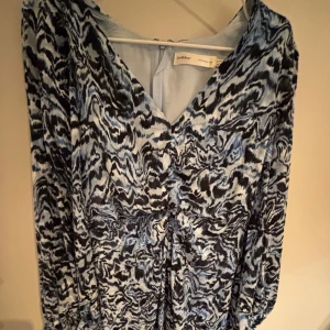 Mönstrad blå klänning från InWear - Supersnygg klänning från InWear med blått och svart abstrakt mönster. V-ringad framtill och långa ärmar. Lätt och flowigt tyg som känns skönt mot huden. Perfekt för dig som vill sticka ut med en cool look.