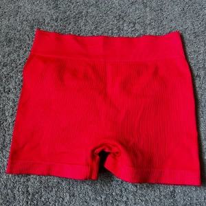 Röda seamless shorts i ribbad modell - Röda seamless träningsshorts i ribbad stretchig modell med hög midja. Materialet är 88% nylon och 12% elastan vilket gör dem riktigt bekväma och följsamma. Baksidan har scrunch-detalj för extra form. Perfekta för träning. Använda en gång❤️