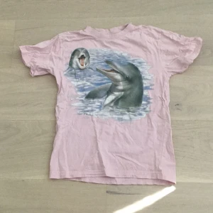 Rosa t-shirt med delfintryck - Söt rosa t-shirt från James & Nicholson med tryck av två delfiner i vatten på framsidan. Klassisk passform med rund hals och korta ärmar. Perfekt för dig som gillar djur och vill ha en chill och unik look. Nypris: 399 kr🫶🏼