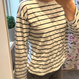 Randig långärmad tröja i bomull - Vit långärmad tröja med svarta horisontella ränder. Klassisk och enkel design med rund halsringning. Tillverkad i mjuk bomull, perfekt för en avslappnad och stilren look. Passar bra till jeans eller kjol för en chill vardagsstil.