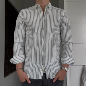 Randig skjorta från Zara i linne - Snygg vit skjorta från Zara med gröna vertikala ränder och relaxed fit. Skjortan är tillverkad i linne, har långa ärmar och klassisk krage. Perfekt för en chill och stilren look. Knappar framtill och skön passform.