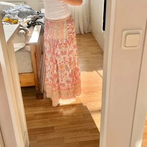Mönstrad långkjol - Såå såå fin långkjol med vackert mönster i rosa/orangea toner. Den är lågmidjad och går hela vägen till golvet för mig som är 166cm lång. Nyskick. Jag köpte kjolen på Lululia för 599kr😙