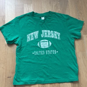 Grön New Jersey t-shirt XS (160)  - Snygg grön t-shirt med vit text 'New Jersey United States' och en amerikansk fotboll på bröstet. Klassisk passform med rund hals och korta ärmar. Perfekt för dig som gillar sportig och avslappnad stil. Köptes från H&M. 