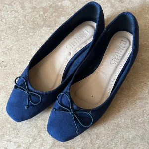 Mörkblå mocka ballerinaskor Lora Ferres - Snygga mörkblå ballerinaskor från Lora Ferres i mjuk mocka med rund tå och liten rosett framtill. Skorna har låg klack och en klassisk, stilren look som passar perfekt till jeans eller klänning.