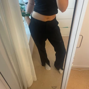 Svarta kostymbyxor med slits nakd  - Snygga svarta kostymbyxor med hög midja och rak, lite loose fit . Perfekta till en stilren outfit och funkar året runt. Jag är 171 och så här sitter dom på mig❣️endast använda 2 gånger.