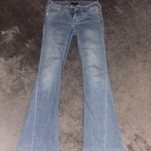 True Religion Joey flare jeans ljusblå - Säljer ett par  True Religion Joey jeans i ljusblå denim med låg midja och bootcut. Klassiska detaljer med broderade bakfickor och silverfärgade knappar. De är uppsydda så de är ca 2cm kortare. Passar mig perfekt som är 1,68
