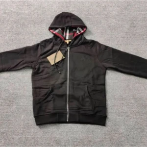 Svart hoodie från Burberry  - Svart hoodie från Burberry i bomull med hel dragkedja, huva med snörning och klassiskt rutigt foder. Broderad Burberry-logga på bröstet och två fickor framtill. Perfekt för dig som gillar stilren streetwear med lyxig touch.