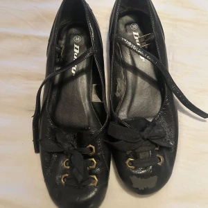 Svarta ballerinaskor från Duffy - Svarta ballerinaskor från Duffy med svarta snören. Spännerna fungerar på båda skorna. Märke på ena skon, men dom är knappt använda.