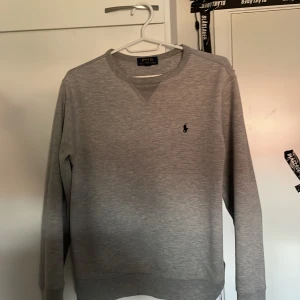  Polo Ralph Lauren sweetshirt - Snygg grå sweatshirt från Polo Ralph Lauren med klassisk rund hals och broderad logga på bröstet. Tröjan har långa ärmar och är tillverkad i mjuk bomull, perfekt för en clean och stilren look.