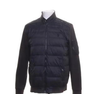 Svart cardigan  från Ralph Lauren - Svart cardigan från Ralph Lauren med quiltad framsida, ribbade muddar och dragkedja. Jackan har ståkrage, fickor med knappstängning och en ärmficka. Perfekt för kyliga dagar och snygg till jeans eller chinos.