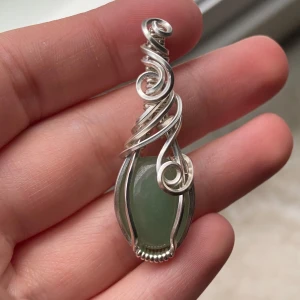 Handgjord silverberlock med grön aventurin. Reserverad!✨  - Unikt halsbandshänge med en grön, slät sten infattad i konstnärligt snirklig silvertråd. Hängsmycket har en organisk, bohemisk känsla och passar perfekt för dig som gillar statement-smycken med naturinspiration. Reserverad!✨