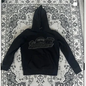 Svarta mjukisbyxor Trapstar Shooters - Svarta mjukisbyxor från Trapstar med broderad Shooters-logga och pantermotiv framtill. Byxorna har resår och snörning i midjan samt muddar vid bensluten. Perfekta för en chill och street-inspirerad look.