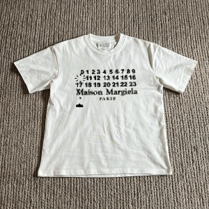 Maison Margiela vit t-shirt - Vit t-shirt från Maison Margiela med ikoniskt svart tryck framtill med siffror och logga. Tillverkad i mjuk bomull och har de typiska fyra stygn bak i nacken. Skick: 10/10, Hör gärna av er vid funderingar, mvh