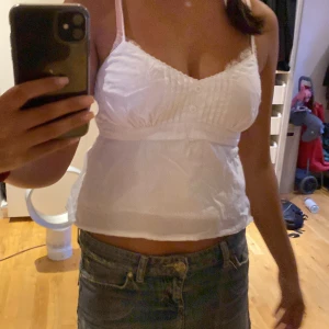 Vit linnetopp från Hollister XS - Supersöt vit linnetopp från Hollister. Toppen har smala axelband, knappar framtill, fina veckdetaljer och spetskant vid bysten. Bra skick.
