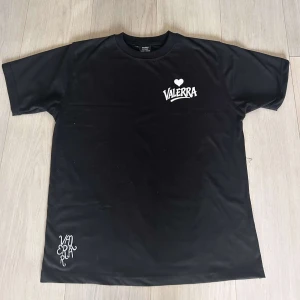 Svart Valerra t-shirt med tryck - Svart t-shirt från Valerra med vit logga och hjärta på bröstet samt tryck nere vid fållen. Klassisk rund hals och korta ärmar. Perfekt för en clean och stilren look.