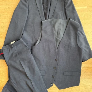 Hugo Boss, mörkblå tredelad kostym - Hugo Boss tredelad kostym, kavaj, väst, byxor. Mörkblå, stl 48. Använda ett fåtal gånger, bla till bröllop. Byxorna behöver läggas upp på nytt samt att en kemtvätt är på sin plats (byxor framförallt). 