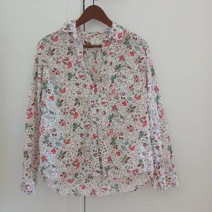 Blommig skjorta från Gap, S - Supersöt skjorta från Gap med blommigt mönster i rött, grönt och brunt på vit botten. Klassisk krage, knäppning framtill och långa ärmar. Skjortan är i bomull och har en relaxed boyfriend fit som är både snygg och bekväm.