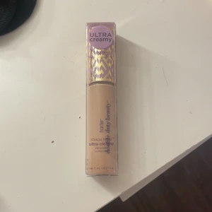 Tarte Shape Tape Ultra Creamy Concealer - Tarte Shape Tape Ultra Creamy Concealer i en ljus beige nyans. Kommer i en snygg tub med lila och guldigt mönster på locket. Ger 24 timmars återfuktning och är både cruelty free och vegansk. Perfekt för att täcka mörka ringar och ojämnheter.