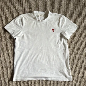 Vit Ami Paris T-shirt - Säljer denna fina T-shirten från Ami som är sjukt skön att ha på sig och lätt. Den är i storlek S och skick är typ 8/10. Hör gärna av er om ni har några ytterligare frågor🏌️🏌️