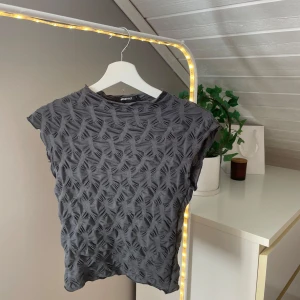 Grå topp med struktur från Gina Tricot - Säljer en grå topp från Gina Tricot i storlek XS. Toppen har ett strukturerat mönster över hela tyget och är ärmlös med rund hals. 