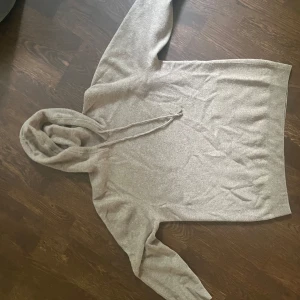 Beige stickad hoodie med snörning - En merino ull hoodie med huva och snörning. Tröjan har långa ärmar och ribbade muddar vid huva och nederkant. Perfekt för en kylig sommarkväll eller för hösten och vintern. Köpt för 899 kr.Passar mer än M än L. Pris kan diskuteras vid snabb försäljning. 