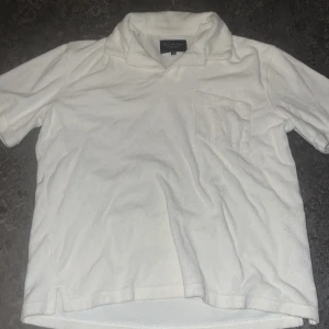 Vit piké t-shirt från Bondelid - Vit piké t-shirt från Bondelid i klassisk stil med krage och bröstficka. T-shirten är kortärmad och tillverkad i mjuk bomull, perfekt för en clean och enkel look. Passar dig som gillar stilrena basplagg med en twist.