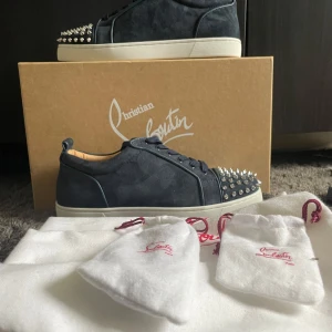 Christian Louboutin sneakers med nitar - Mörkblå sneakers i mocka från Christian Louboutin med vita sulor och ikonisk röd undersida. Skorna har snörning och är dekorerade med silvriga nitar på tån för en edgy look. Perfekta för dig som vill sticka ut med exklusiva detaljer. Box ingår ej❗️