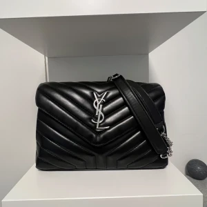 Ysl väska  - Säljer en så fin och I princip oanvänd YSL väska i svart & silver. Super bra skick med många fack som du får plats med mycket saker. YSL Box & kvitto och påse medföljer! Hör av er vid fler bilder eller frågor så löser jag det 💞säljer pågrund av ingen användning då jag mer är en guld tjej 🫰