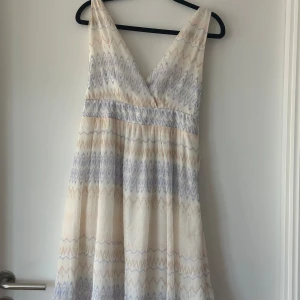 Långklänning från Vila med pastellmönster - Supersöt långklänning från Vila i ljusa pastellfärger med vågigt mönster i lila och beige. Djup v-ringning fram och omlott i ryggen med knytband. Klänningen passar även de som bär M och S. Då jag sj när S och den sitter bra! Helt ny och oanvänd!