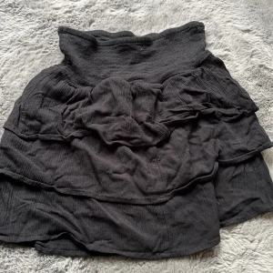 Svart volangkjol från BikBok XS - Supersöt svart kortkjol från BikBok i storlek XS. Kjolen har flera lager volanger och bred smock i midjan för en bekväm passform. Tillverkad i ett mjukt, lätt bomullstyg som ger en avslappnad vibe. Perfekt att styla med en croppad topp eller hoodie.