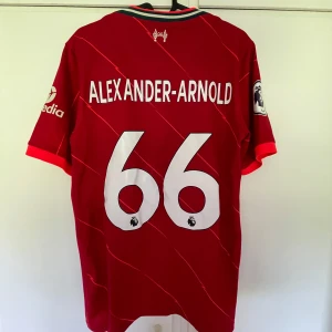 Liverpool Alexander-Arnold tröja Nike S - Liverpool FC matchtröja från Nike med Alexander-Arnold och nummer 66 på ryggen. Röd med tunna diagonala linjer, vita loggor och detaljer. Kortärmad modell i lätt funktionsmaterial, Premier League-märke på ärmen och sponsortryck framtill.