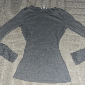 Grå långärmad tröja i bomull - En enkel och stilren grå långärmad tröja i mjuk bomull. Tröjan har en rund halsringning och en figurnära passform som passar perfekt till jeans eller kjol. Perfekt basplagg för garderoben.