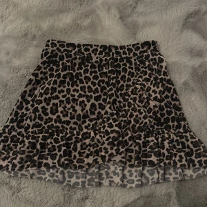 Leopardmönstrad volangkjol från Lindex - Superfin kort kjol från Lindex med leopardmönster i svart och beige. Kjolen har volangkant nertill och omlott-look framtill. 